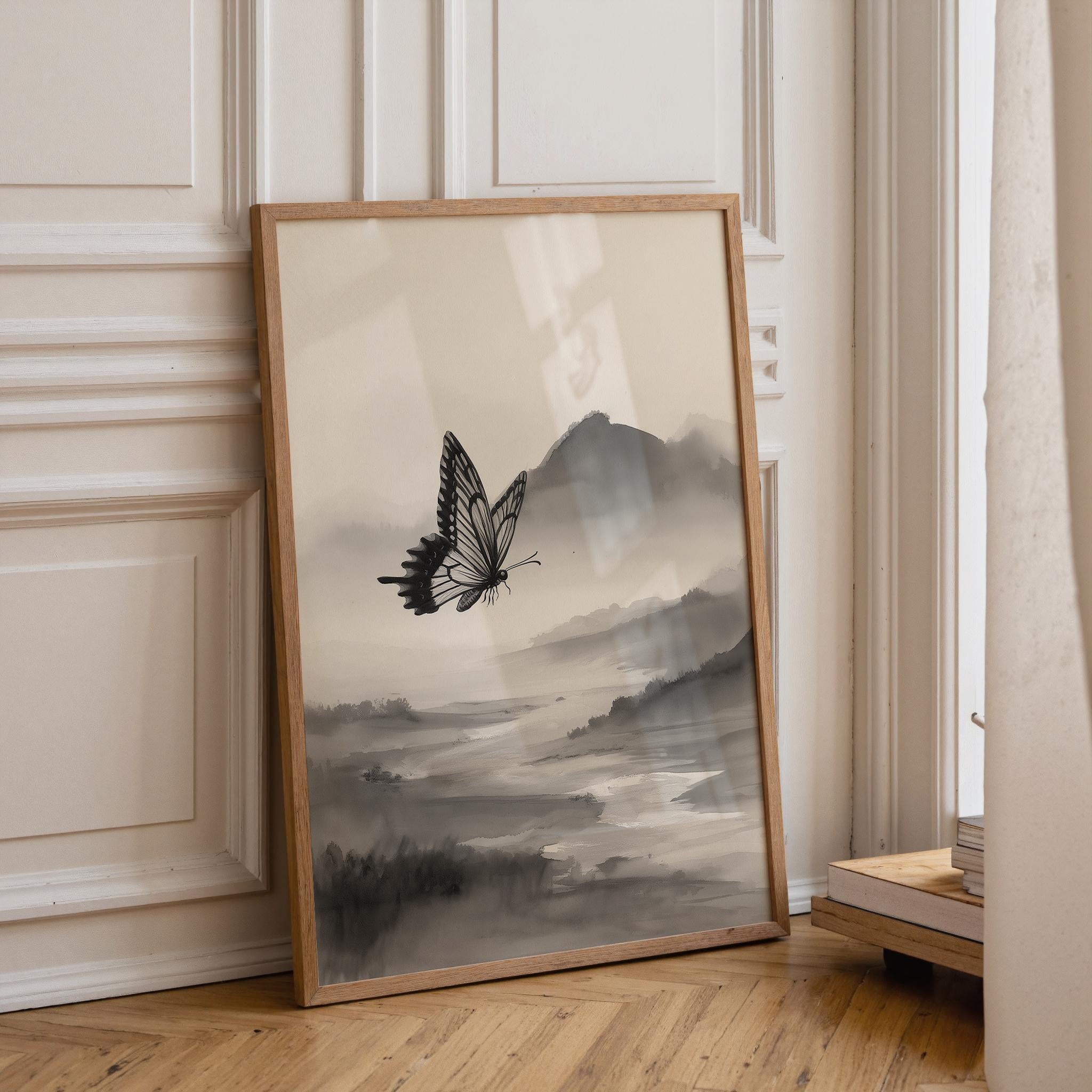 A framed art print featuring a black and white butterfly over a misty mountain landscape, leaning against a cream paneled wall on a light wood floor.