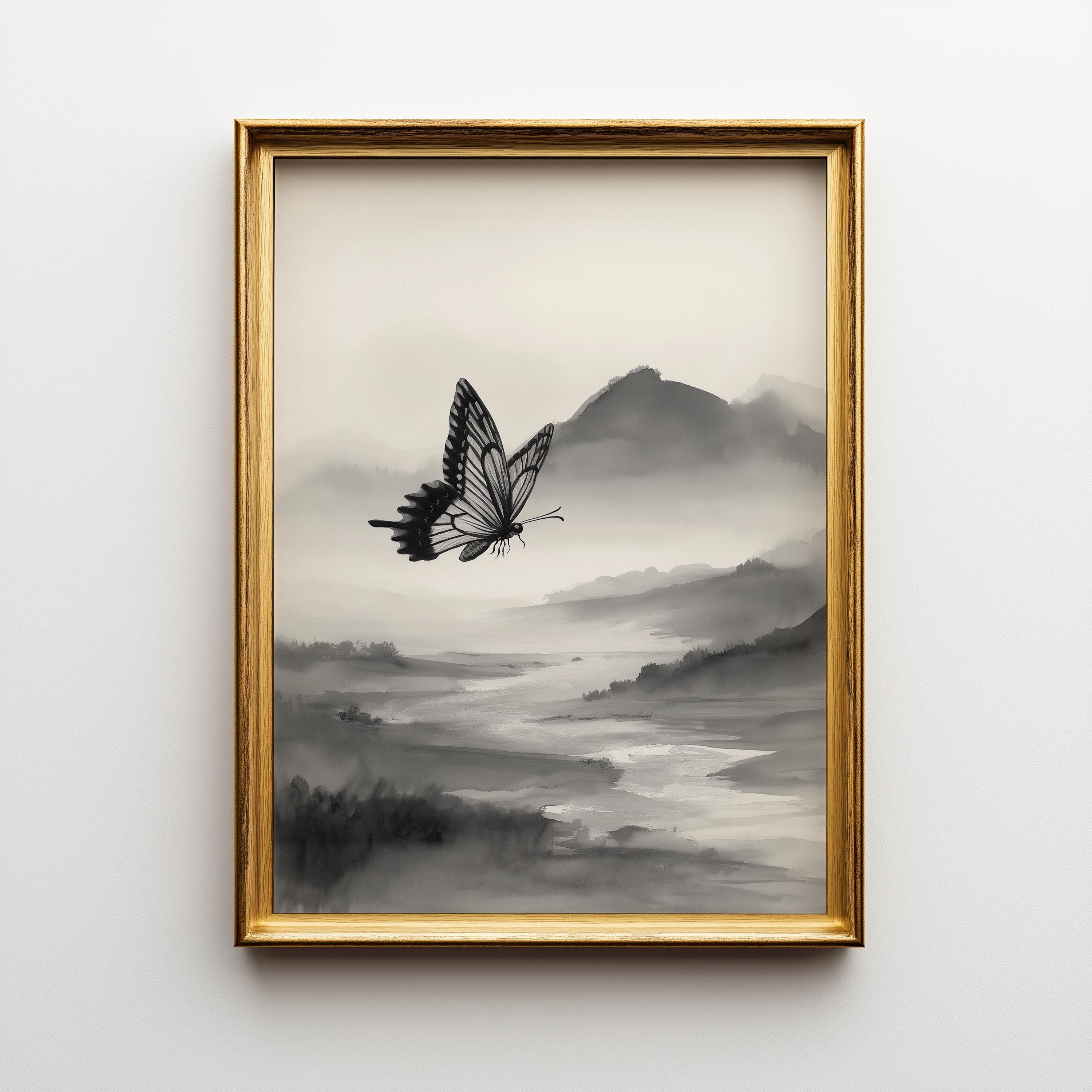 Framed wall art featuring a black butterfly over a misty gray landscape with layered hills and a pale river, displayed in a gold frame against a light gray wall.