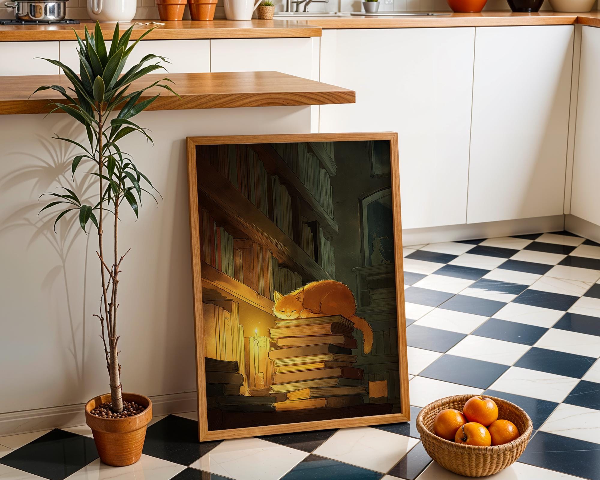A framed art print depicting a cozy orange cat resting on stacked books under warm candlelight, leaning against a kitchen wall on a black-and-white checkered floor next to a potted plant and a basket of oranges.